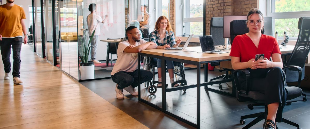 A diverse group of business professionals collaborates in a modern startup coworking center, utilizing a mix of paper-based and technological tools such as mobile phones and computers .